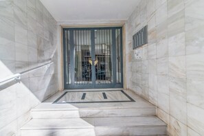 Eine Marmortreppe führt zu einem verschlossenen Eingang mit einem Metallgitter und einer Lüftungseinheit an der Wand.