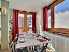 Ein Essbereich mit einem für zwei Personen gedeckten Tisch, einem Fenster mit Blick auf eine verschneite Landschaft und einer Holztür mit Blick auf ein Gebäude.