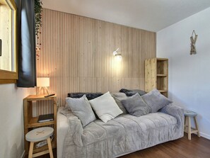 Ein gemütliches Wohnzimmer mit grauem Sofa, einem Holz-TV-Schrank, einem kleinen Hocker und einer Holzregaleinheit.