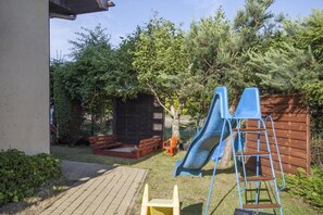 Ein Garten mit einer Rutsche, einer Holzterrasse und einer Ziegelwand.