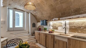 A kitchen with wooden cabinets, a stone wall, a built-in oven, and a window with a view. - La Cummarizza - Le Case di Valentina (Gallipoli)