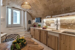 A kitchen with wooden cabinets, a stone wall, a built-in oven, and a window with a view. - La Cummarizza - Le Case di Valentina (Gallipoli)