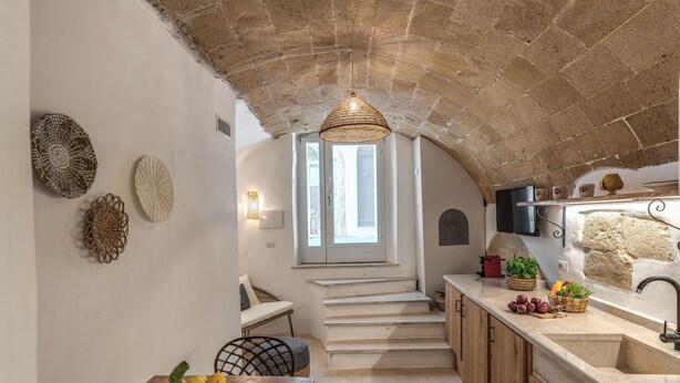A kitchen with a stone ceiling, a wooden table with lemons, and a basket of vegetables. - La Cummarizza - Le Case di Valentina (Gallipoli)