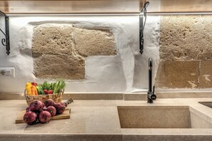A kitchen with a stone backsplash, a sink, and a fruit basket on the counter. - La Cummarizza - Le Case di Valentina (Gallipoli)
