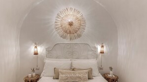 A bedroom with a white bed, a decorative ceiling light, two bedside lamps, and a round wooden side table with a vase. - La Cummarizza - Le Case di Valentina (Gallipoli)