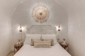 A bedroom with a white bed, a decorative ceiling light, two bedside lamps, and a round wooden side table with a vase. - La Cummarizza - Le Case di Valentina (Gallipoli)