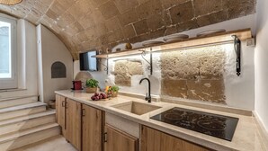 A kitchen with a stone wall, wooden cabinets, a double sink, and a built-in stove. - La Cummarizza - Le Case di Valentina (Gallipoli)