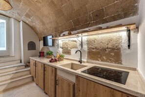 A kitchen with a stone wall, wooden cabinets, a double sink, and a built-in stove. - La Cummarizza - Le Case di Valentina (Gallipoli)