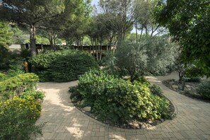 A landscaped garden with a paved walkway, various shrubs, and trees. - Sea Apartments Alghero (Alghero (SS))