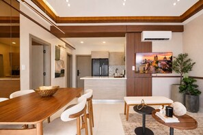 A modern kitchen with a central island, a dining area with a wooden table and chairs, and a living area with a bench and a small side table. - ®{Niza~City~Tower} @DowntownSD +Pool+Gym+Balcony (Santo Domingo)