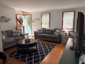 A living room with two sofas, a coffee table, and a TV. There are windows with blinds, a rug, and a lamp. - Cozy Classic Cape - Minutes to Eastham Beaches (Eastham)