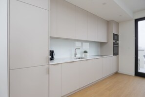 A modern kitchen with white cabinets, a stainless steel countertop, a sink, and a built-in oven. - Spacious Apartment | Parking | Air Conditioning | Workspace. (Warszawa)