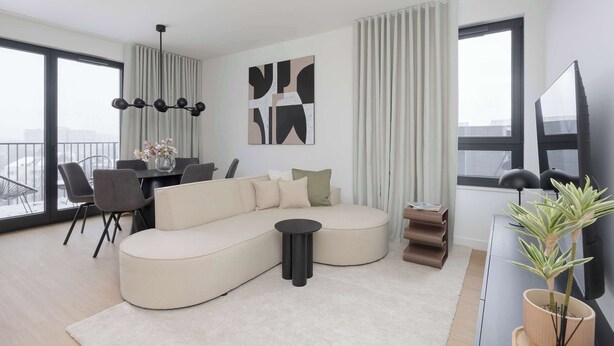 Una sala de estar moderna con un sofá modular, una mesa de comedor con sillas, una mesita auxiliar negra, una planta en maceta y un amplio ventanal con cortinas.