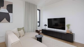 Una sala moderna con un sofá, una mesa redonda para café, un televisor sobre un mueble negro, una planta en maceta y un cuadro abstracto grande en la pared.