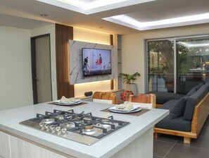 A modern kitchen with a central island, a flat-screen TV mounted on the wall, and a sliding glass door leading to a balcony. - An Experience of Luxury and Comfort (Medellín)
