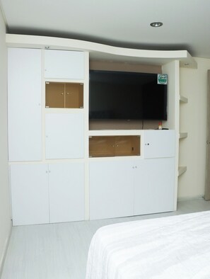 A bedroom with a bed, a white wardrobe with multiple compartments, and a television mounted on the wall. - An Experience of Luxury and Comfort (Medellín)