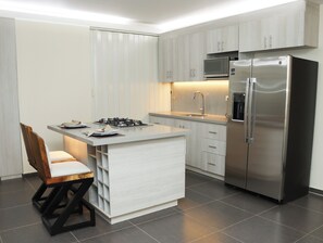 Una cocina moderna con una isla central, electrodomésticos de acero inoxidable y un comedor con una silla.