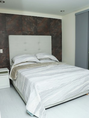 Ein modernes Schlafzimmer mit einem großen Bett, einem Nachttisch und einer Kopfteil an einer Wand mit marmorartiger Struktur.