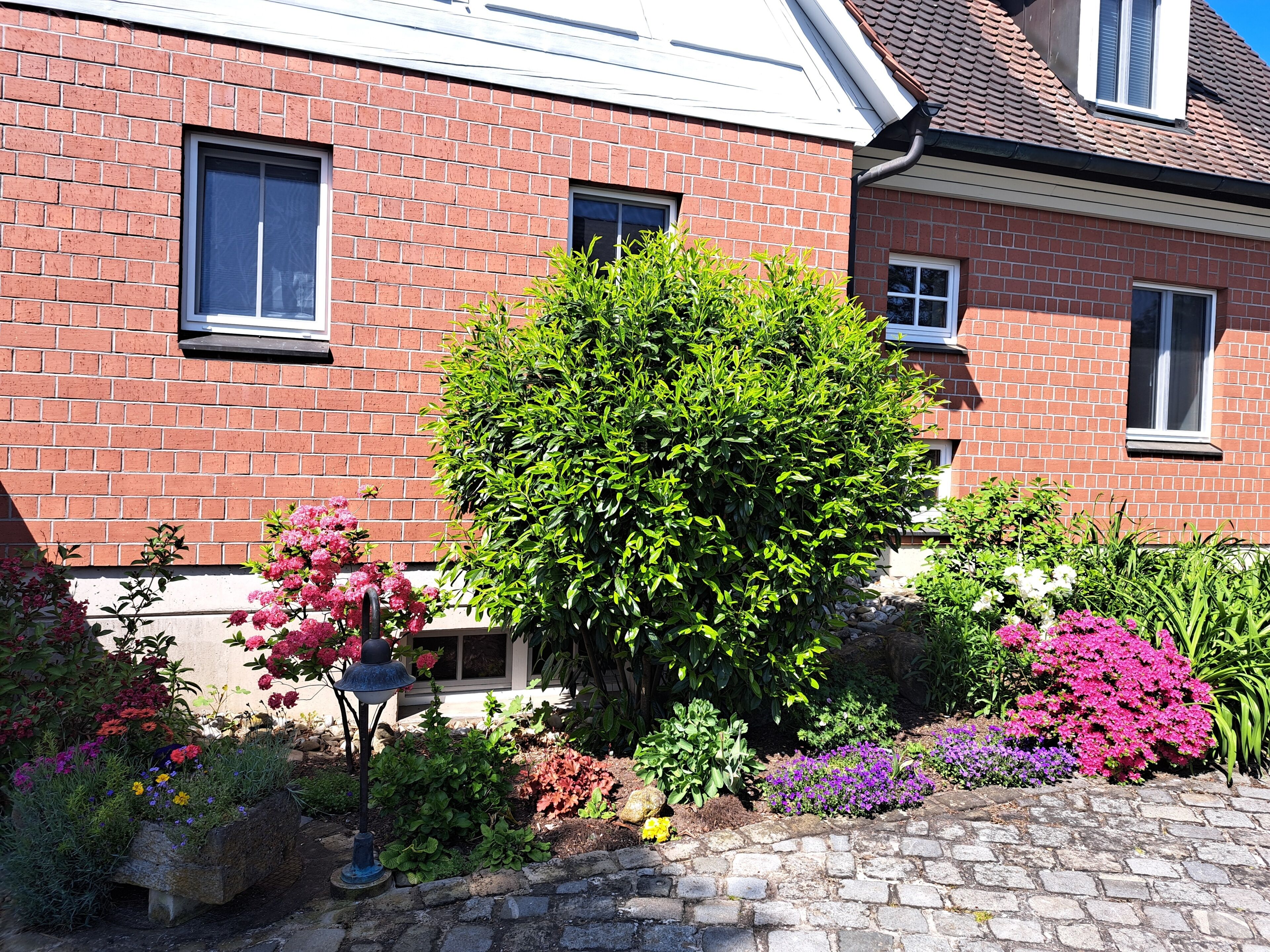 Ein Gebäude aus roten Ziegeln mit einem gepflegten Garten, einem Pflasterweg und einer Straßenlaterne.