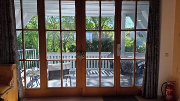 Ein Zimmer mit einer großen Schiebeglasdoor, die auf eine Terrasse mit weißer Geländer und einem Tisch führt.