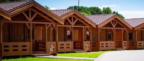 A row of wooden cabins with pitched roofs, each with a porch and a door.