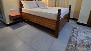 A bedroom with a wooden bed, a nightstand, a wall-mounted light, and a patterned rug. - Al-mendhiry Apartment (Zanzibar)