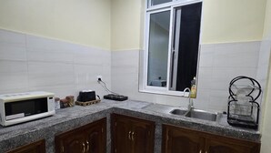A kitchen with granite countertops, wooden cabinets, a microwave, a sink, and a window. - Al-mendhiry Apartment (Zanzibar)