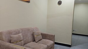 A room with a sofa, a ceiling fan, a painting, and a door. - Al-mendhiry Apartment (Zanzibar)