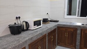 A kitchen with granite countertops, wooden cabinets, a microwave, a kettle, and a stove. - Al-mendhiry Apartment (Zanzibar)