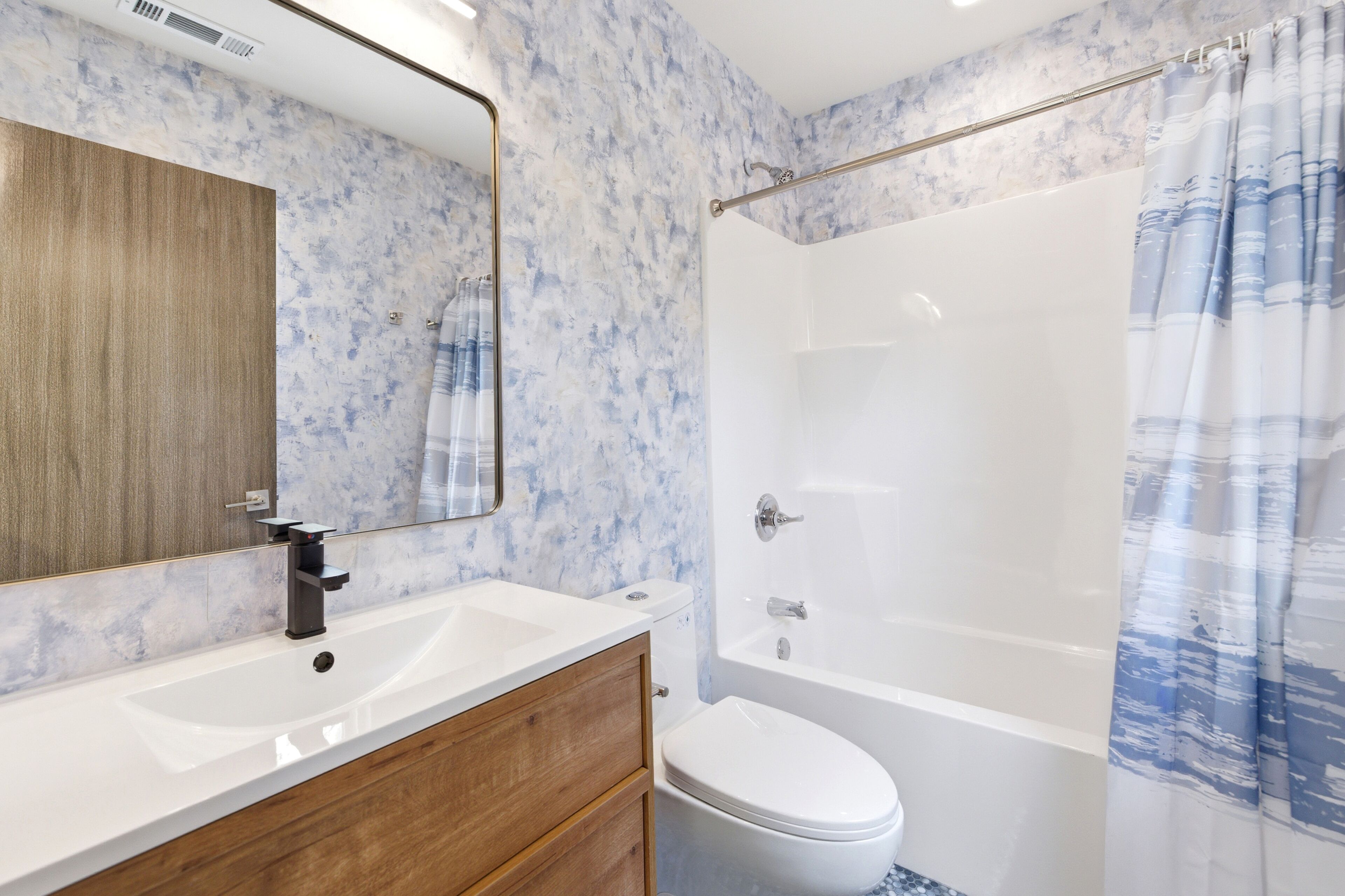 A bathroom with a white sink, wooden vanity, a white toilet, and a bathtub with a shower curtain.