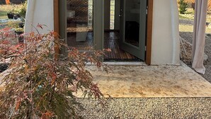A modern, triangular-shaped building with a glass door entrance, surrounded by a gravel pathway and some foliage. - Private Spa & Yurt with Sauna, Soaking Tub - Glamp & Walk to Main St (Murphys)