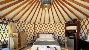 A spacious tent with a bed, a wooden chest, a small table, a microwave, and a refrigerator. - Private Spa & Yurt with Sauna, Soaking Tub - Glamp & Walk to Main St (Murphys)