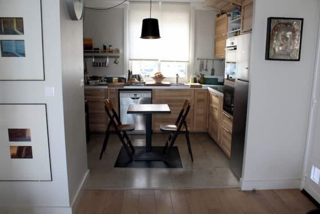 A modern kitchen with wooden cabinets, a dining table with chairs, and a hanging pendant light.
