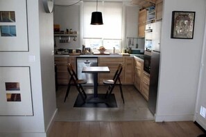 Eine moderne Küche mit Holzausstattung, einem Esstisch mit Stühlen und einer hängenden Pendelleuchte.