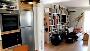 Eine Küche mit modernen Geräten, ein Essbereich mit einem Stuhl und ein Wohnzimmer mit einer Couch und Bücherregal.