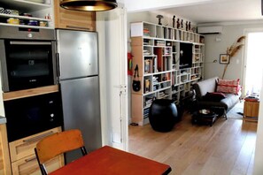 Eine Küche mit modernen Geräten, ein Essbereich mit einem Stuhl und ein Wohnzimmer mit einer Couch und Bücherregal.