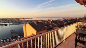 Blick auf das Meer vom Balkon mit Geländer, eine Marina mit Booten und einem wolkenlosen Himmel.
