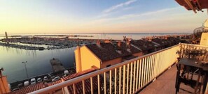 Blick auf das Meer vom Balkon mit Geländer, eine Marina mit Booten und einem wolkenlosen Himmel.