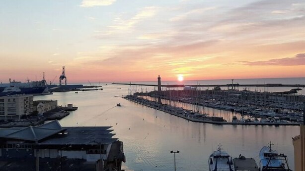 Ein Yachthafen mit vertäuten Booten, eine Pier, die sich ins Wasser erstreckt, und ein Gebäude mit einem geneigten Dach.