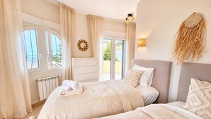 Ein Schlafzimmer mit zwei Betten, einem Heizkörper, einem Fenster mit Vorhängen, einer Wandleuchte und einem Wandbild.