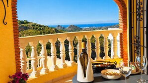 Ein Balkon mit Blick auf das Meer, ein Tisch mit Flasche, Gläsern und einer Oliven-Schale.