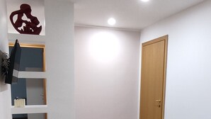 A room with a wooden floor, a dark-colored sofa, a wooden door, and a wall-mounted shelf with a red decorative item. - Eve's House. Up to 4 guests. Opposite the subway station (Roma)