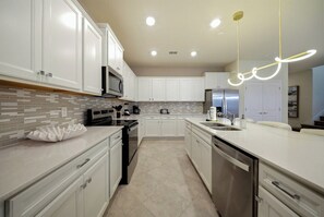 Welcome to this bright kitchen featuring sleek white cabinetry and a spacious island, ideal for your culinary adventures. With modern appliances and a stylish tile backsplash, this space invites you to create and enjoy delicious. - 10BR house sleeps 28 near Disney area (Clermont)