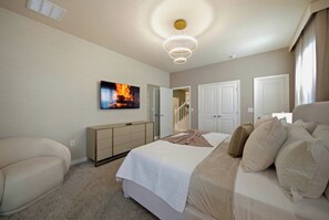 Experience a cozy bedroom with a plush king-size bed, soft linens, a stylish bedside table, and a modern TV mount. The warm neutral tones and elegant chandelier offer a welcoming atmosphere perfect for relaxation. - 10BR house sleeps 28 near Disney area (Clermont)
