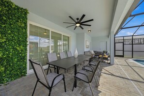 Step outside to a spacious dining area where sleek black chairs surround a stylish table, ideal for alfresco meals. Enjoy the natural greenery and the comfort of a ceiling fan, perfect for any gathering. - 10BR house sleeps 28 near Disney area (Clermont)