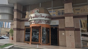 A building with a sign in Arabic, a glass entrance, and a potted plant outside.