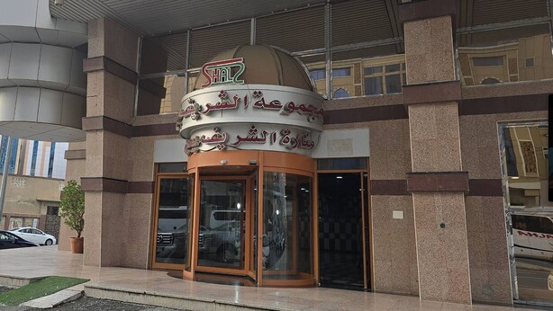 A building with a sign in Arabic, a glass entrance, and a potted plant outside. - Apartment in Makkah (Makkah)
