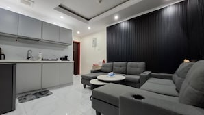 A modern living room with a grey sofa, a coffee table, and a kitchen area with grey cabinets and a white countertop.
