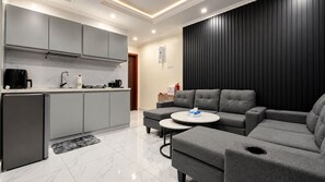 A modern living room with a grey sofa, a small round coffee table, and a kitchen area with grey cabinets and a black refrigerator.