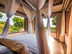 Un dormitorio con una cama grande, cortinas translúcidas y vista a zonas verdes.